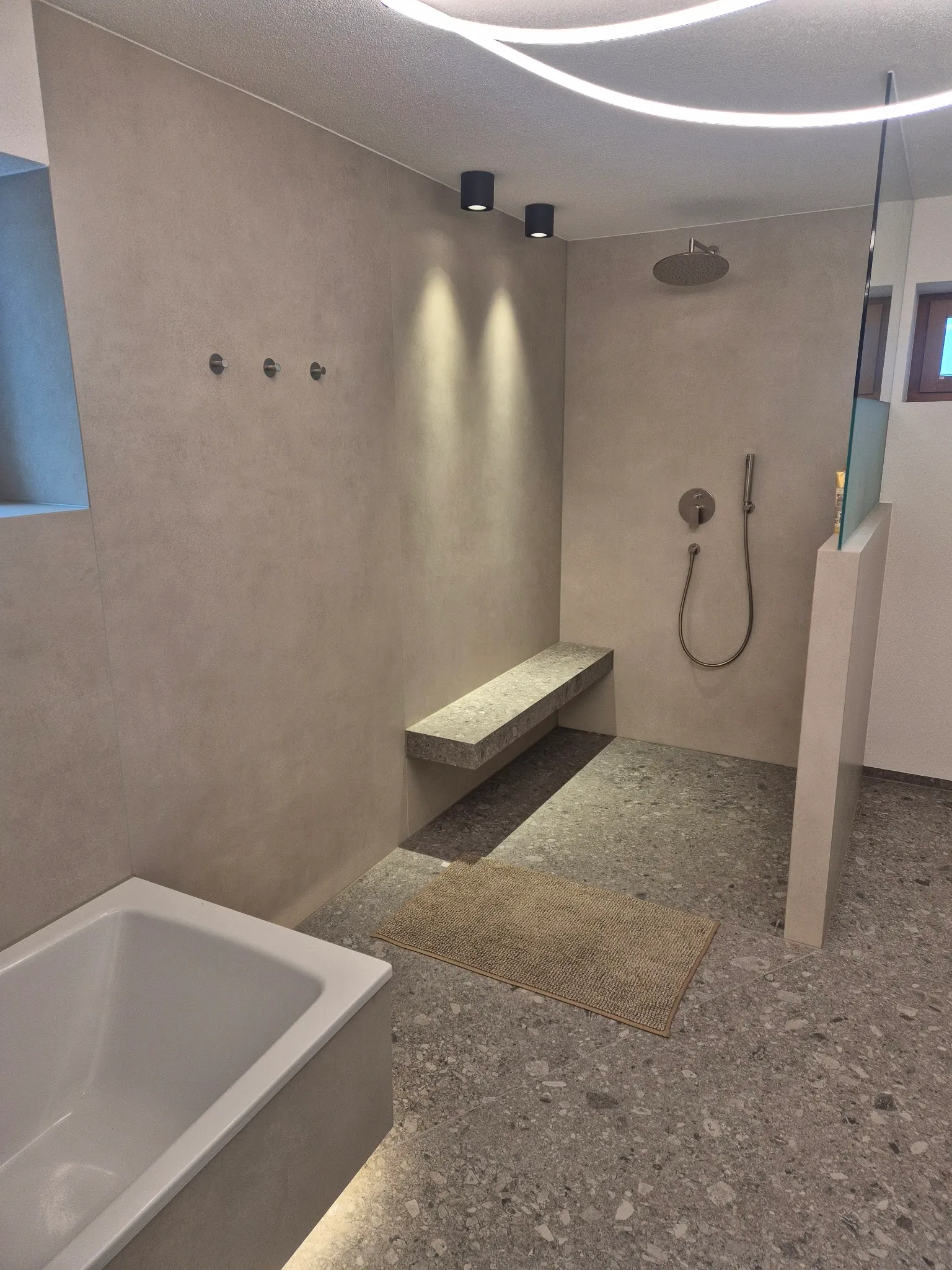Bad mit bodengleicher Dusche, geflieste Sitzbank und Badewanne, großformatige graue Platten