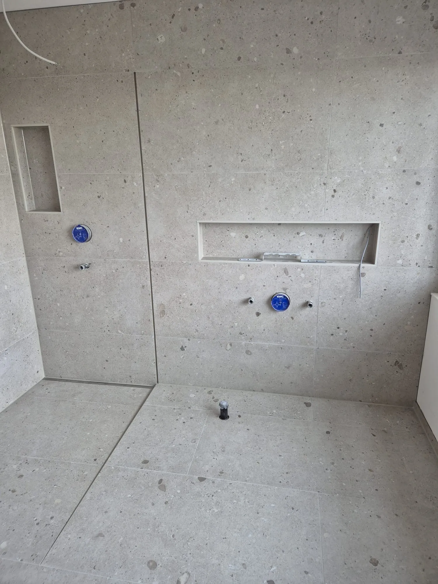 Dusche im Rohzustand mit Terrazzo-Großformaten an Wand und Boden, Wandnischen