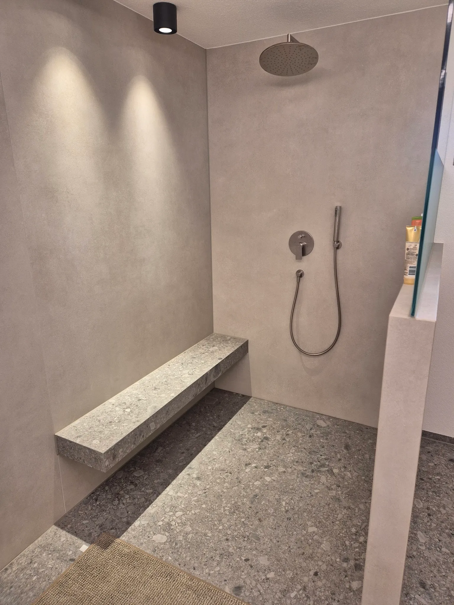Dusche mit großformatigen grauen Wandplatten und Sitzbank aus Terrazzo