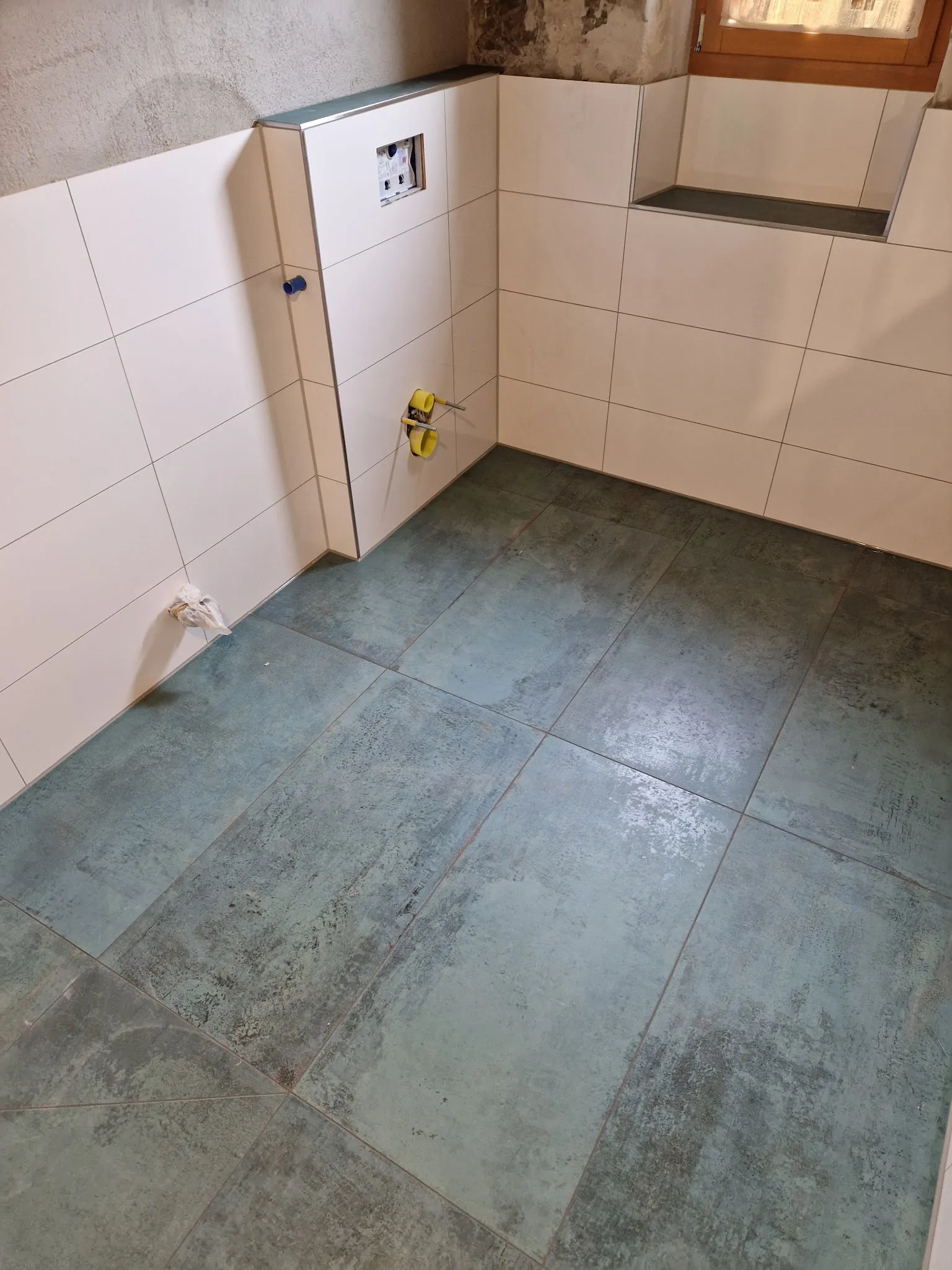 Bad mit grünem Steinboden, hellen Wandfliesen und Ablage am Fenster